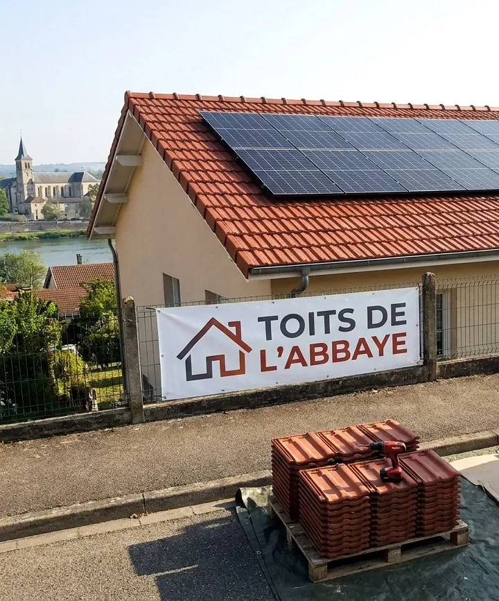 Toiture en tuiles mécaniques terminée par Les Toits de l'Abbaye à Pont-à-Mousson, bâche de l'entreprise sur la clôture, abbaye des Prémontrés et Moselle au fond